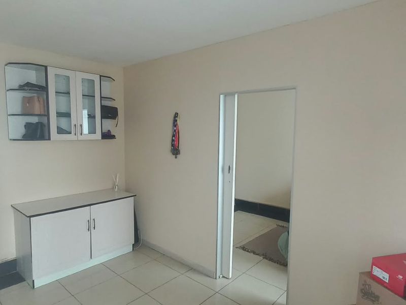 A living area featuring tiled flooring and built-in cabinetry, providing a functional space with direct access to an adjacent room and exterior area.