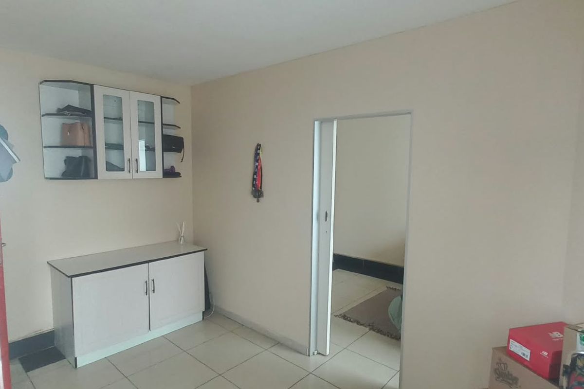 A living area featuring tiled flooring and built-in cabinetry, providing a functional space with direct access to an adjacent room and exterior area.