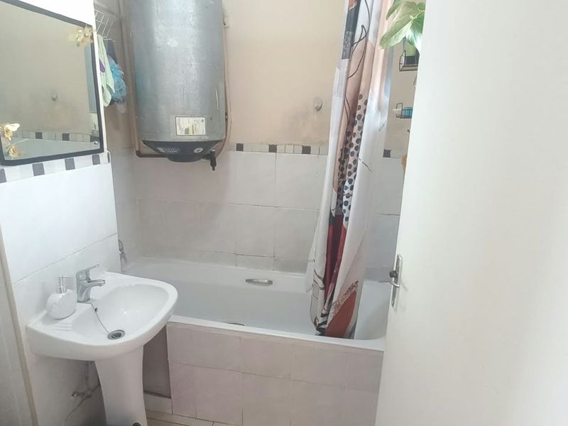 A functional bathroom featuring a pedestal basin, bathtub, and wall-mounted electric geyser, requiring cosmetic updates to improve its overall condition and aesthetic appeal.