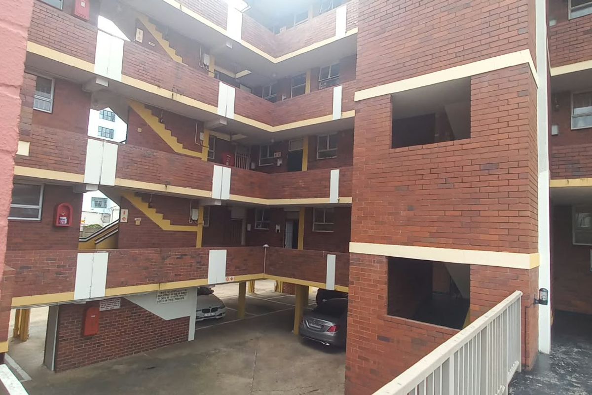 Exterior view of a multi-story apartment complex featuring face brick construction, open-air stairwells, and ground-level covered parking facilities.