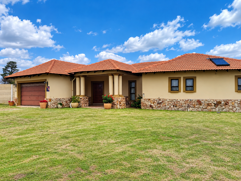 A well-maintained single-story house featuring a terracotta tiled roof, stone cladding accents, a double garage, and a covered entrance with decorative columns.