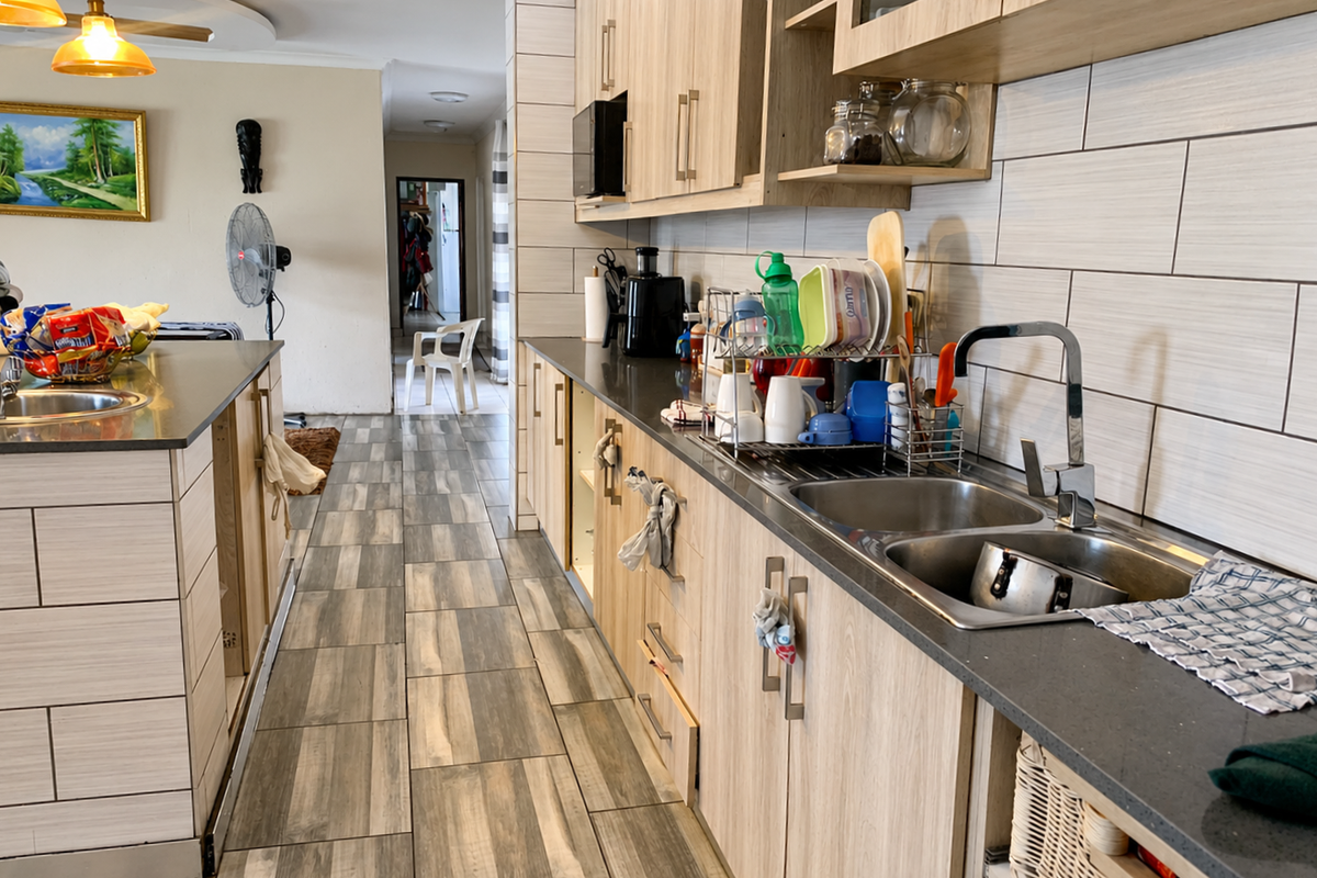 A modern kitchen featuring light wood-tone cabinetry, stone countertops, a double stainless steel sink, and contemporary tiled backsplash and flooring.