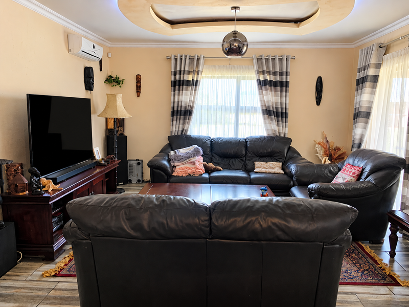 A comfortable living room featuring a decorative recessed ceiling, tiled flooring, and a wall-mounted air conditioning unit.