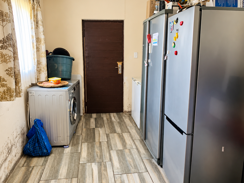 A functional laundry area featuring tiled flooring and plumbing connections, currently showing signs of significant wall dampness and surface wear requiring maintenance.