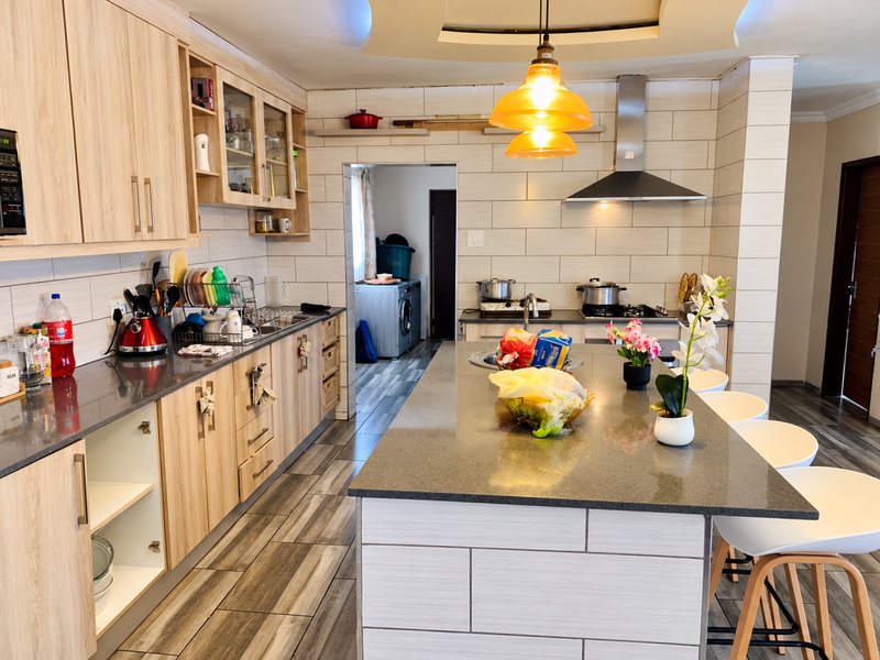 Modern kitchen featuring light wood cabinetry, stone countertops, a central island with breakfast bar seating, and integrated appliances with stylish pendant lighting.