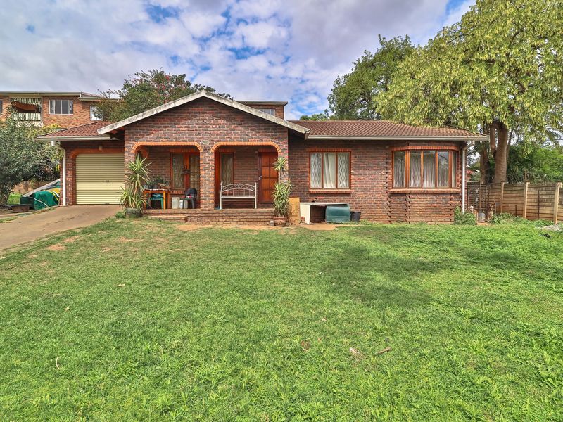 A single-story face brick house featuring a covered front porch, a garage, and a bay window, set on a large grassed plot.