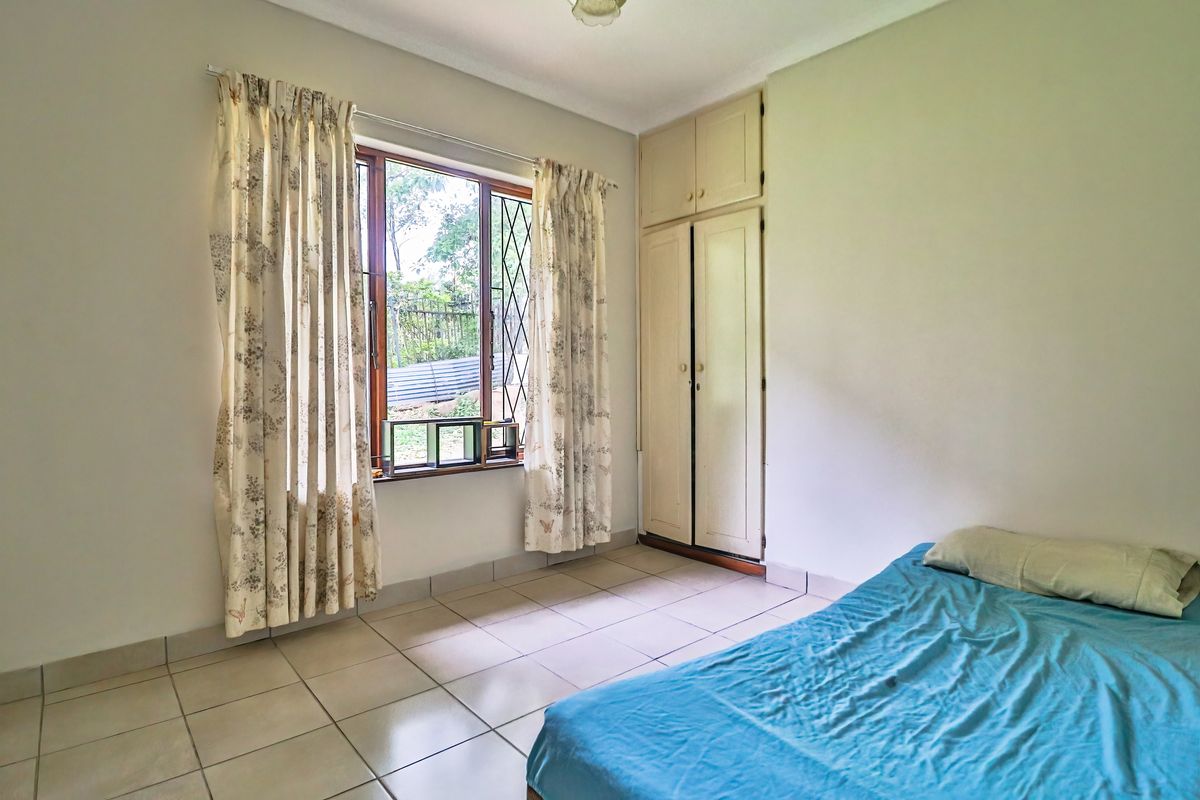 A functional bedroom featuring tiled flooring, built-in cupboards, and a window with security bars, offering a neutral base for potential updates.