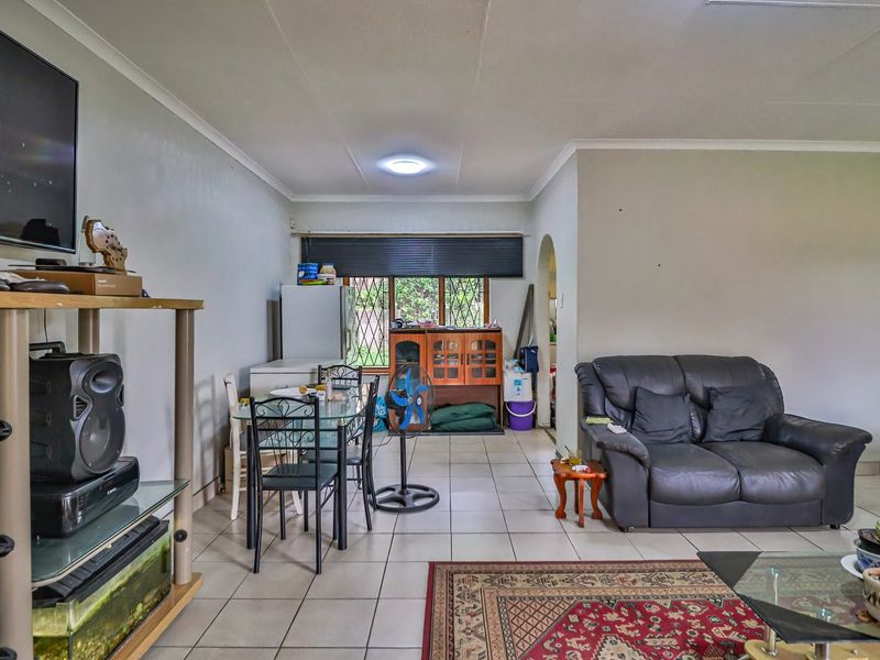 Open-plan living and dining area featuring tiled flooring, coved ceilings, and security-barred windows, offering a functional layout for daily living.