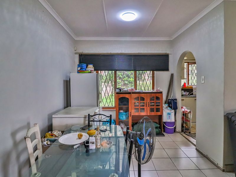 Dining area featuring tiled flooring and an arched entryway leading to the kitchen, with natural light provided by a window with fitted blinds.