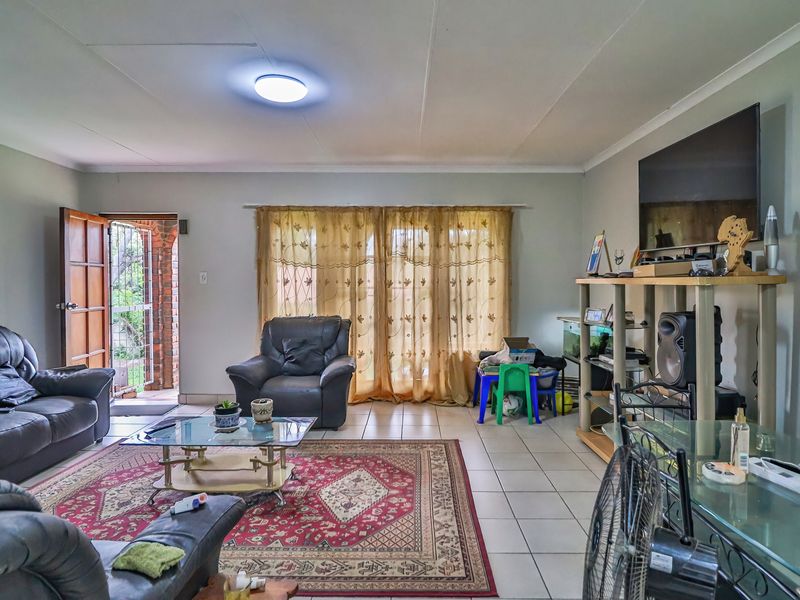 Spacious living room featuring neutral wall tones, tiled flooring, and direct access to the exterior through a sliding glass door with security gate.