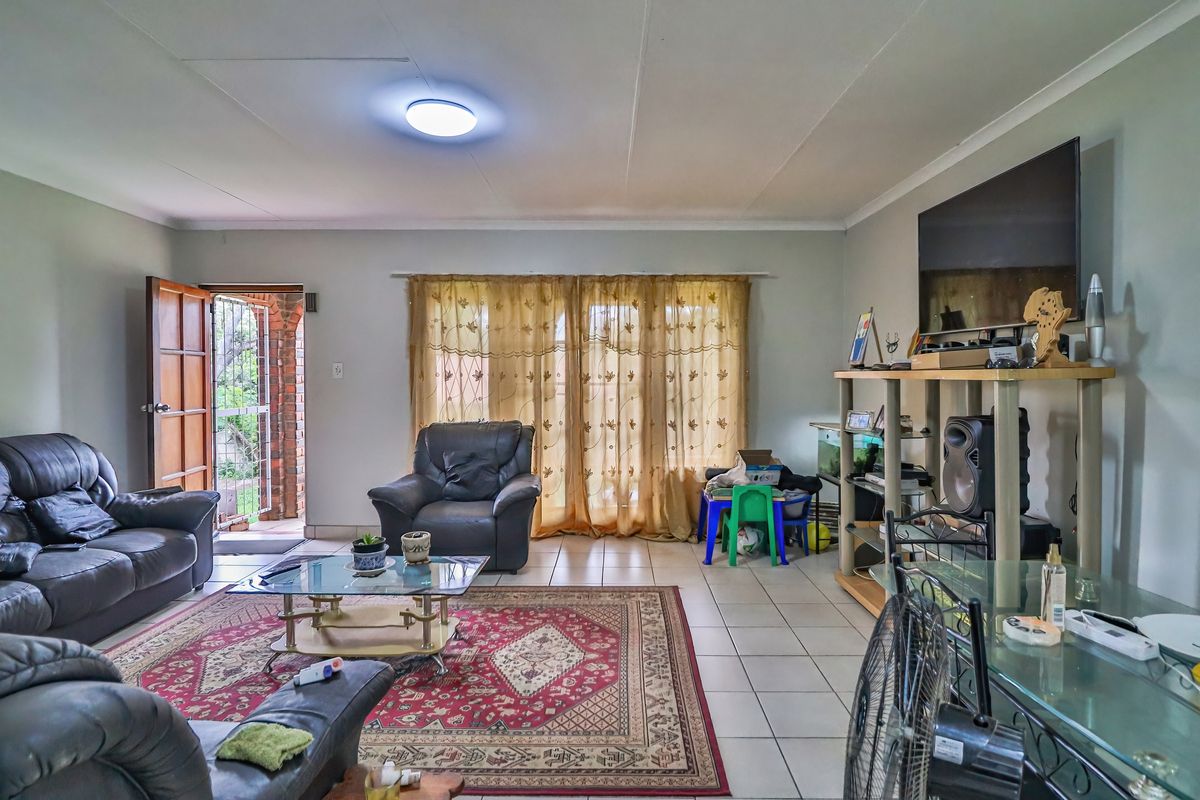 Spacious living room featuring neutral wall tones, tiled flooring, and direct access to the exterior through a sliding glass door with security gate.
