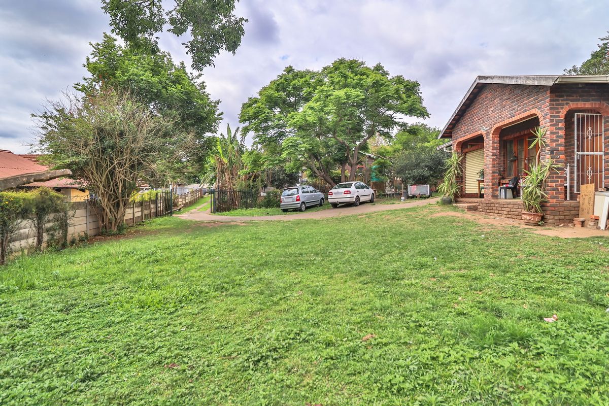 Spacious rear garden featuring a brick-faced house with a covered patio area and established trees.
