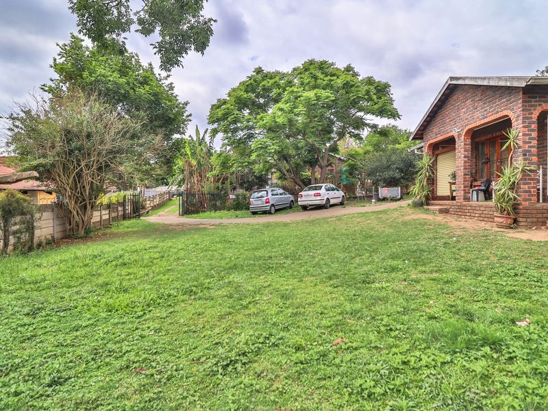 Spacious rear garden featuring a brick-faced house with a covered patio area and established trees.