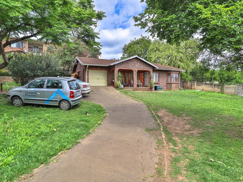 Front view of a single-story face brick house featuring a tiled roof, a single garage, and a concrete driveway set on a spacious lawn.