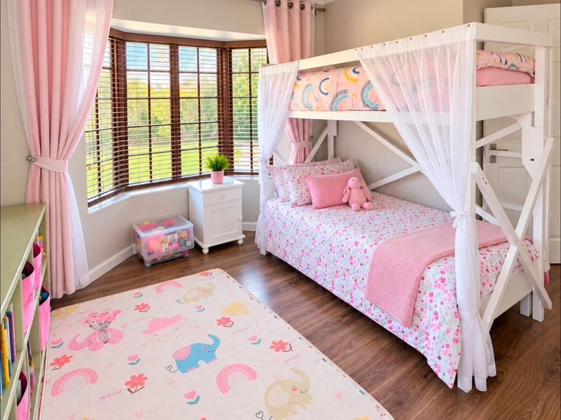 A bright and well-maintained bedroom featuring a large bay window, laminate flooring, and a ceiling fan.