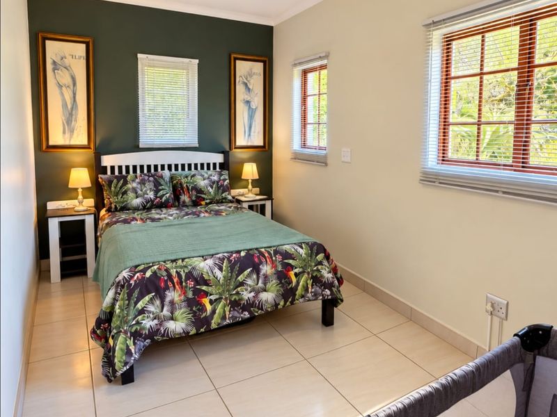 A well-lit bedroom featuring tiled flooring, a ceiling fan, and a dark green accent wall with dual windows.