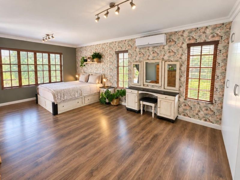 Spacious bedroom featuring laminate flooring, split-system air conditioning, track lighting, and large windows with timber venetian blinds.