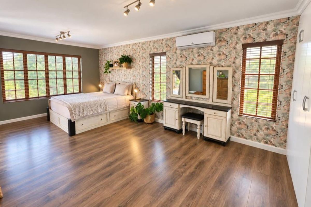 Spacious bedroom featuring laminate flooring, split-system air conditioning, track lighting, and large windows with timber venetian blinds.