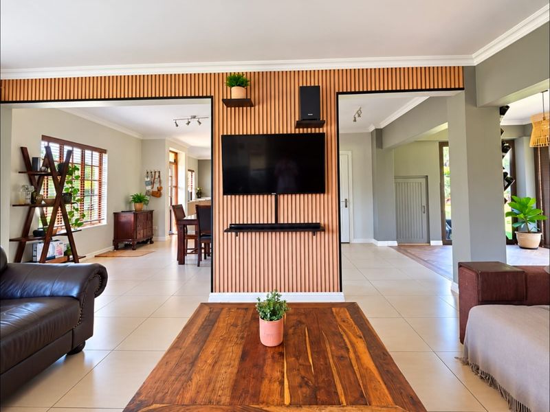 Spacious open-plan living area featuring a modern slatted timber feature wall, neutral tiled flooring, and recessed ceiling lighting with seamless flow to adjacent rooms.