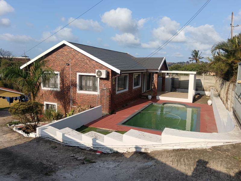 Rear view of a face brick house featuring a swimming pool, covered patio area, and perimeter boundary walling.