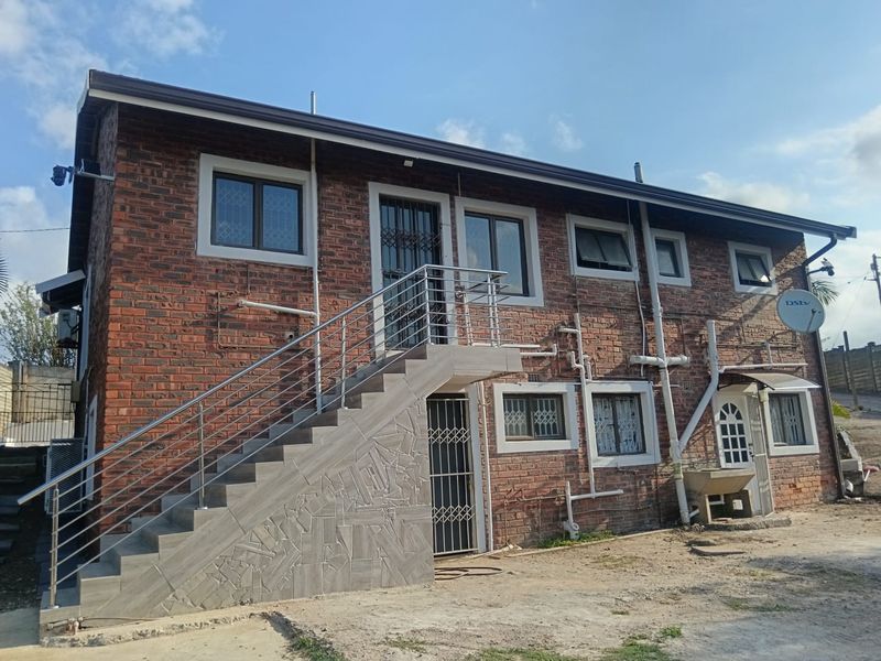 Rear view of a double-story face brick house featuring an external staircase with stainless steel balustrades and multiple security-fitted doors and windows.