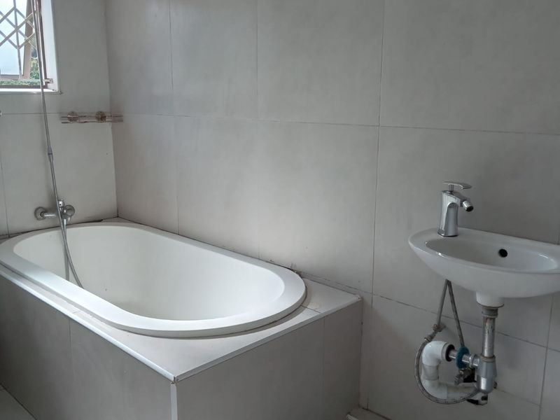 A functional bathroom featuring a built-in bathtub, wall-mounted basin with exposed plumbing, and neutral ceramic tiling throughout.