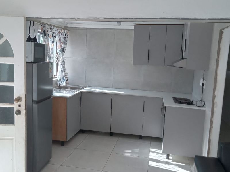A compact kitchen featuring modern grey cabinetry, tiled splashbacks, a built-in hob with extractor, and tiled flooring, offering a functional prep space.