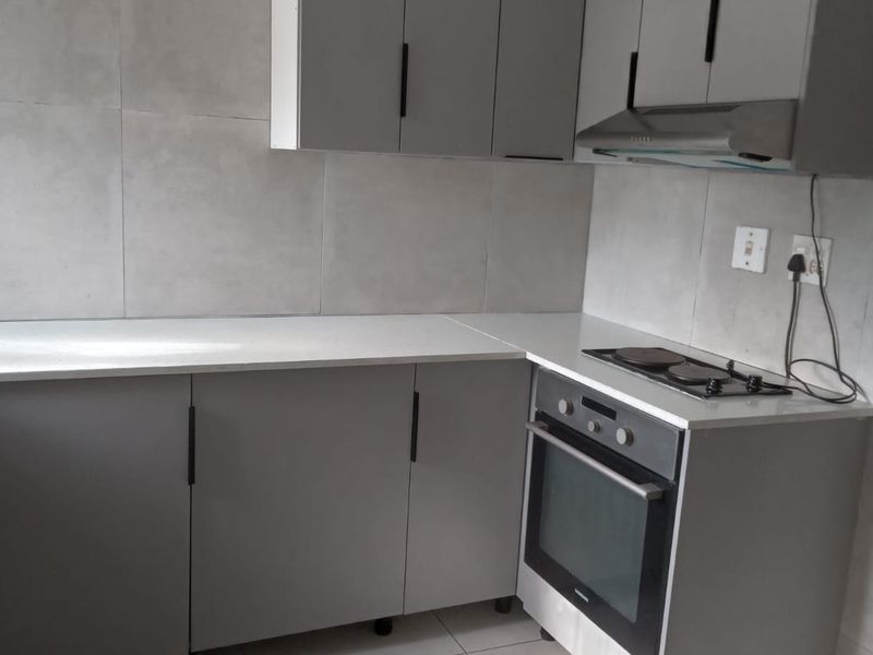 A modern, compact kitchen featuring grey cabinetry, stone countertops, a built-in oven, and an electric hob with an integrated extractor fan.