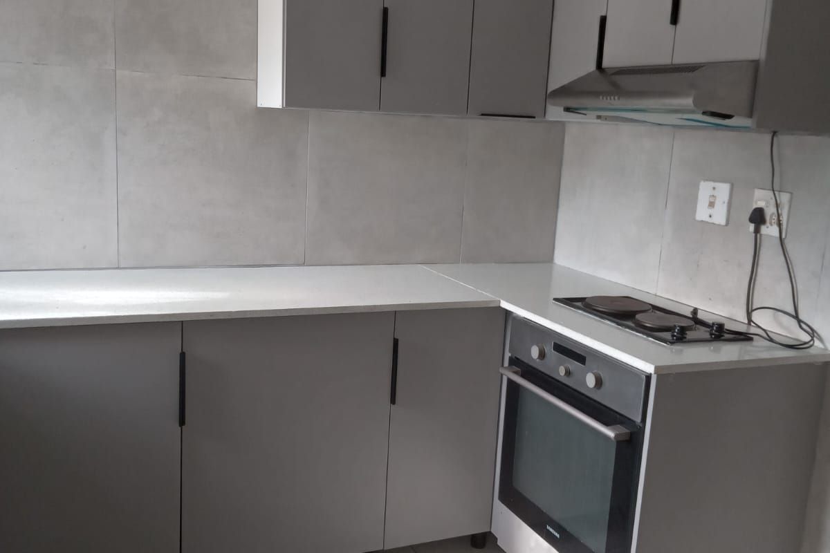 A modern, compact kitchen featuring grey cabinetry, stone countertops, a built-in oven, and an electric hob with an integrated extractor fan.