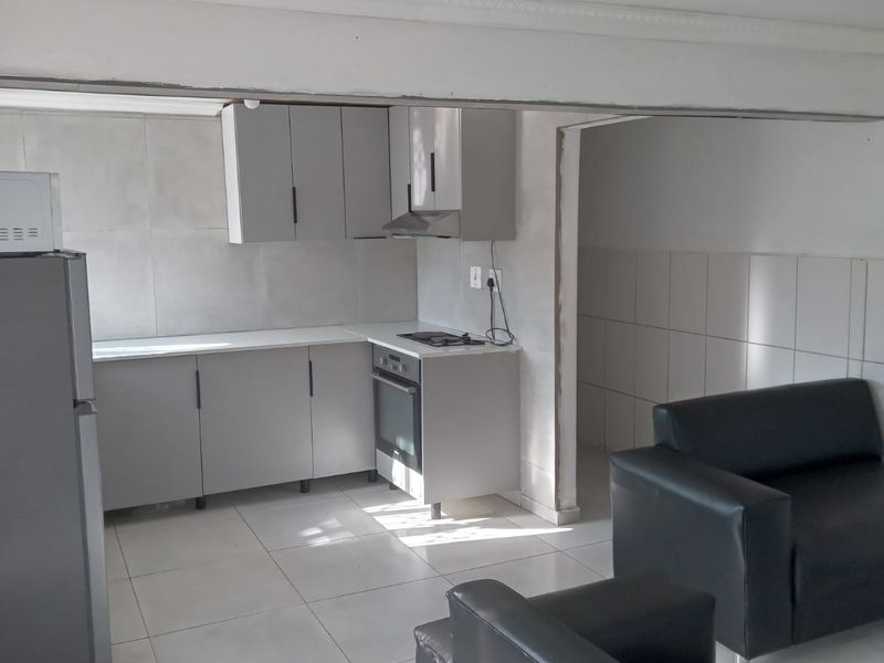 Open plan kitchen and living area featuring modern grey cabinetry, built-in oven, hob, extractor fan, and neutral tiled flooring throughout.