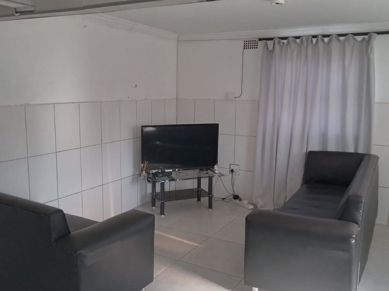 A living room featuring tiled walls and flooring, with visible ceiling cornicing and a curtain rail. The space requires cosmetic updates to improve finishes.