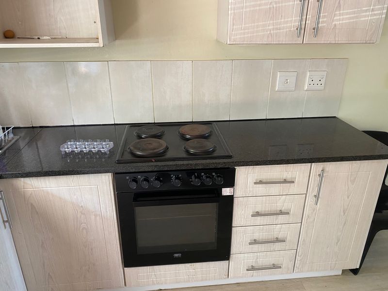 A functional kitchen featuring light wood-grain cabinetry, dark laminate countertops, a built-in electric oven, and a four-plate hob with a tiled backsplash.