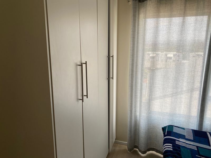 A bedroom featuring a modern white built-in wardrobe with sleek metal handles and light-toned laminate flooring.