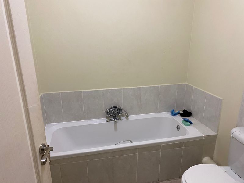 A functional bathroom featuring a built-in bathtub with chrome mixer tap and tiled splashback, alongside a standard toilet.