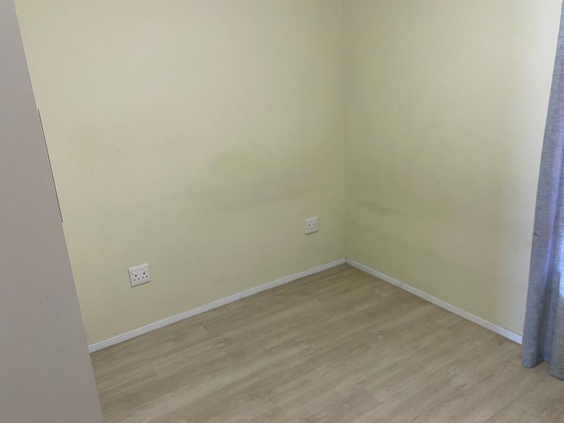 An empty bedroom featuring light-toned laminate flooring and neutral walls with visible scuff marks, ready for personalization.