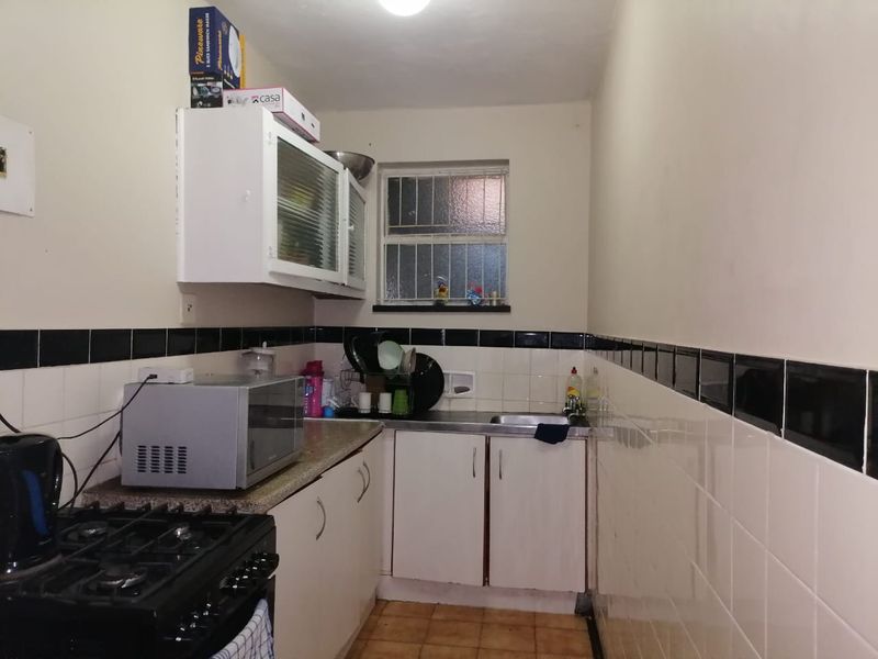A compact kitchen featuring built-in cabinetry, a gas stove, and a stainless steel sink with tiled splashbacks and security bars on the window.
