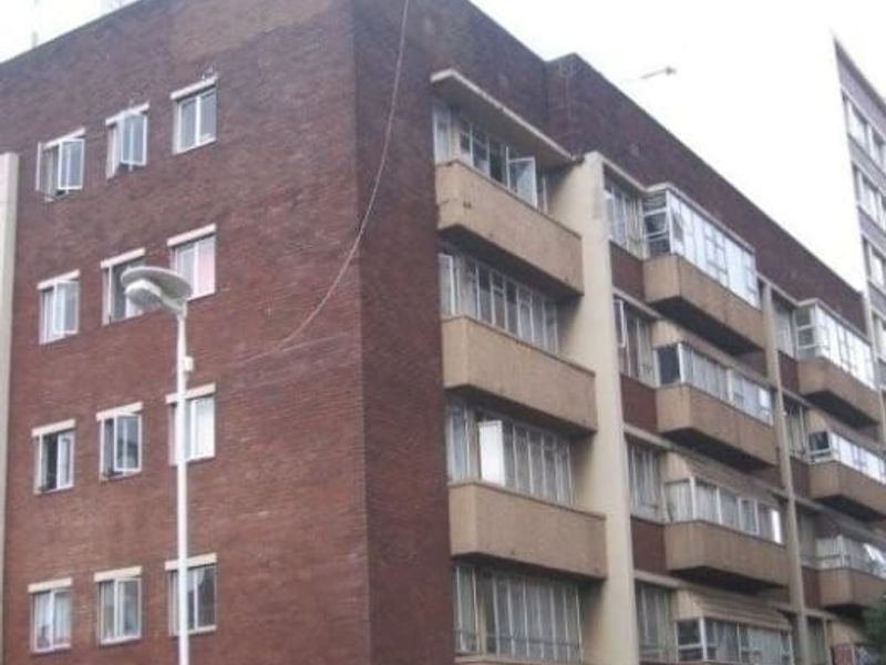 Exterior view of a multi-story brick apartment building featuring multiple balconies and casement windows.