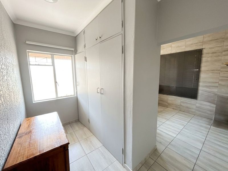A bright bedroom featuring neutral tiled flooring, built-in cupboards, and a clean, minimalist aesthetic with an adjacent tiled space.