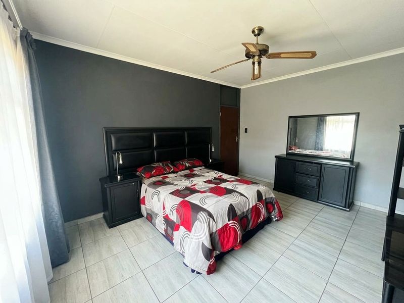 A spacious bedroom featuring neutral tiled flooring, a ceiling fan, and a dark accent wall, providing a clean and functional living space.