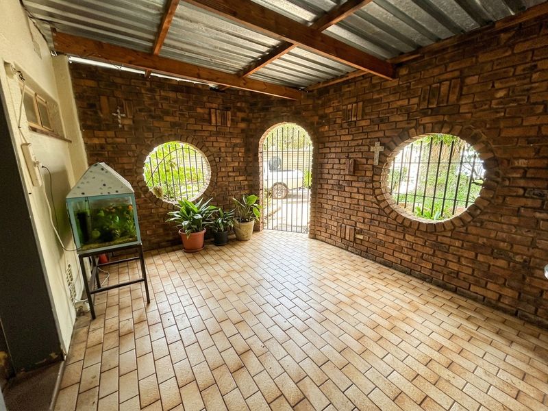 A covered patio area featuring exposed brick walls, circular windows with security bars, and tiled flooring under a corrugated metal roof.