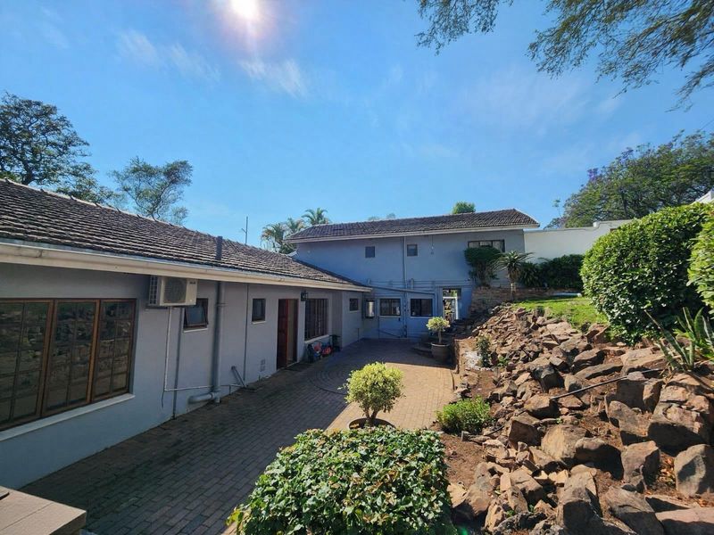 Rear exterior view of the property featuring a paved courtyard, rockery garden, and multi-level building structure with tiled roofing.
