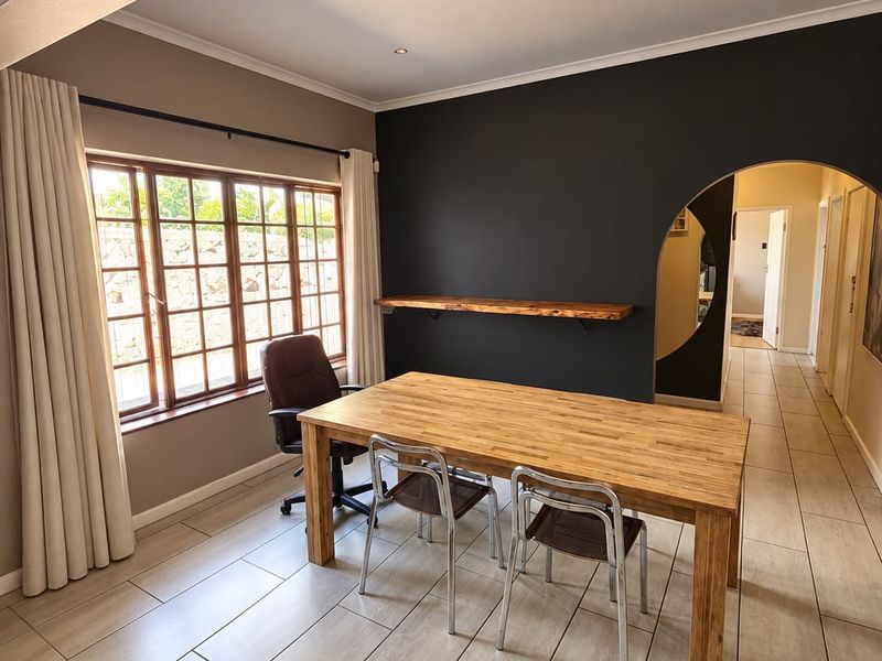 A bright living area featuring tiled flooring, a distinctive arched doorway, and a built-in timber shelf against a dark accent wall.