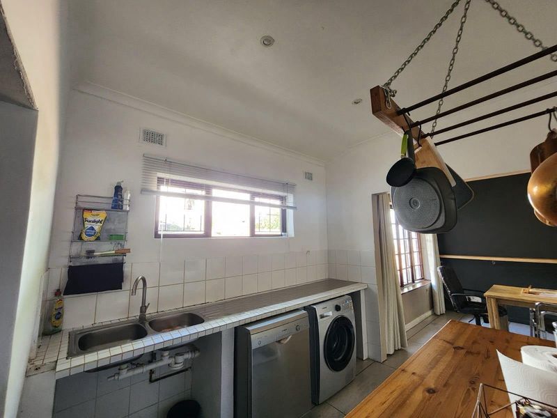 Functional laundry area featuring a double stainless steel sink, tiled countertop, and convenient ceiling-mounted drying rack with integrated plumbing for appliances.