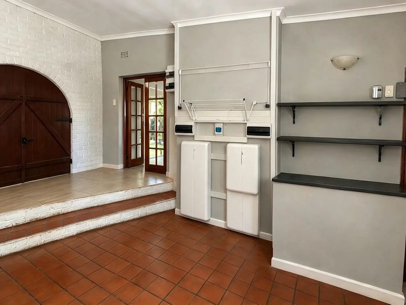 A functional utility space featuring terracotta tile flooring, an arched brick feature wall, and built-in shelving with direct access to the garden.