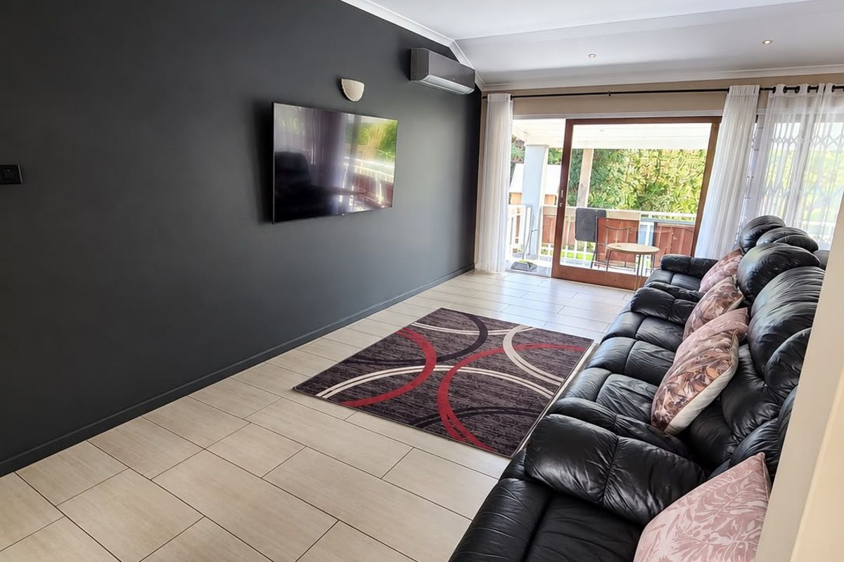 A modern living room featuring tiled flooring, recessed downlights, a wall-mounted air conditioner, and a sliding glass door leading to an outdoor area.
