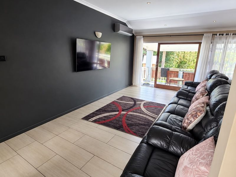 A modern living room featuring tiled flooring, recessed downlights, a wall-mounted air conditioner, and a sliding glass door leading to an outdoor area.