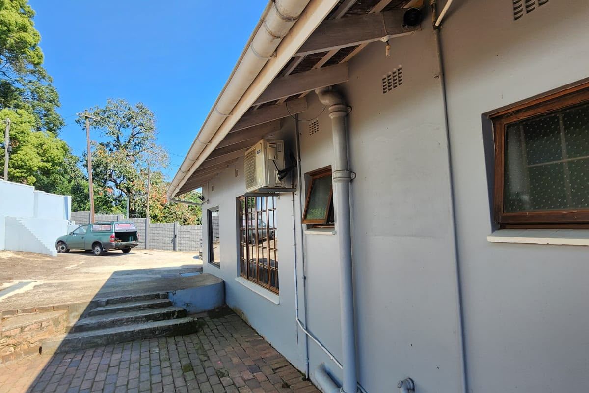 Rear exterior view of the property featuring brick paving, concrete steps, and a side facade with an installed air conditioning unit.