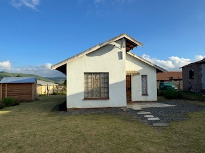 Front view of a detached single-story house with a pitched roof, featuring a concrete pathway and surrounding garden area.