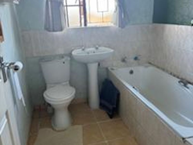 A functional bathroom featuring a pedestal basin, toilet, and bathtub with tiled flooring and wall splashbacks.