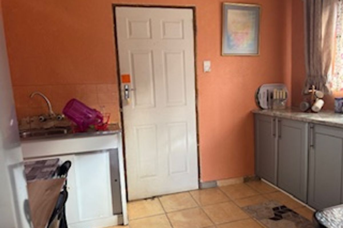 A compact kitchen featuring built-in cabinetry, laminate countertops, and tiled flooring, currently finished in a dated orange wall color.